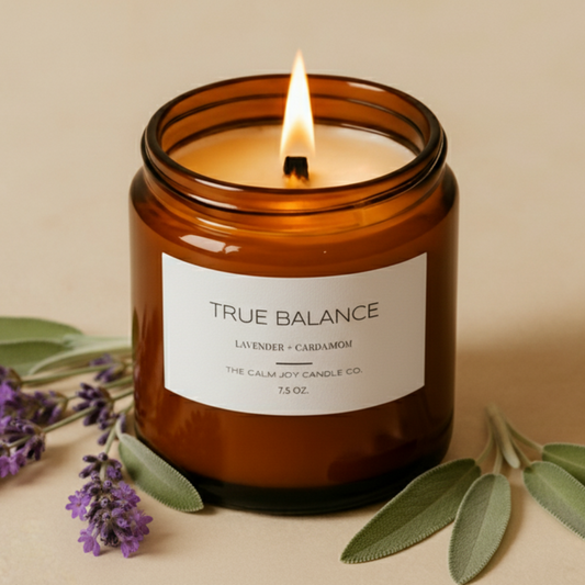 Candle in an amber jar labeled 'True Balance' with lavender and sage leaves on a beige background