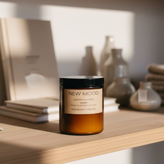 Candle labeled 'New Mood' on a wooden shelf with books, a plant, and other decorative items.