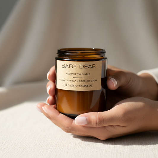 Hand holding a 'Baby Dear' candle with a beige background