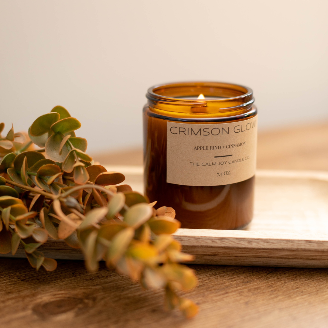 Candle labeled 'Crimson Glow' on a wooden surface with greenery