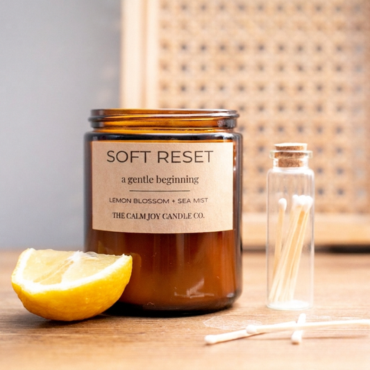 Candle labeled 'Soft Reset' from The Calm Joy Candle Co. with a lemon and matches on a wooden surface.